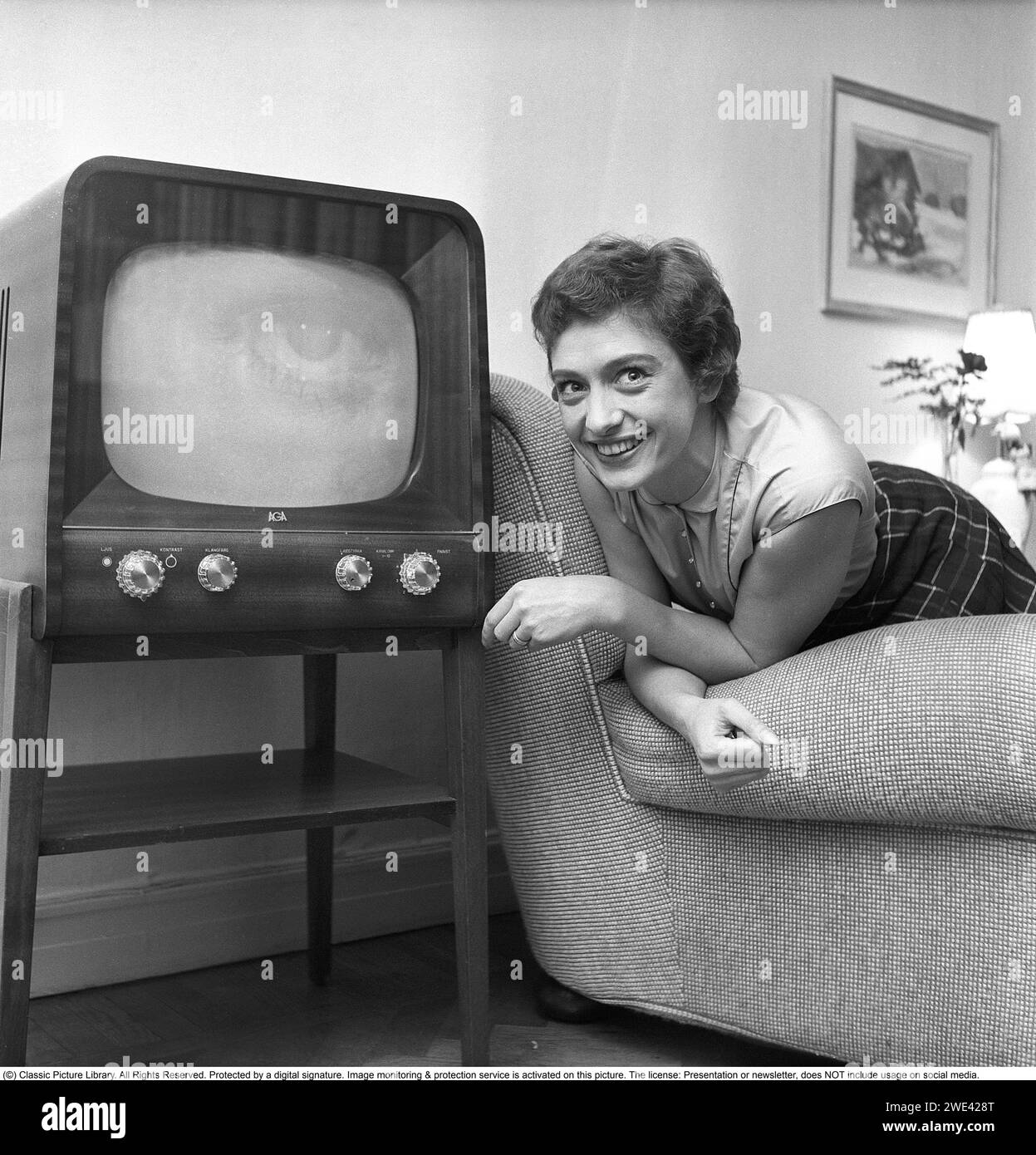 Karin Falck schwedische Regisseurin, Fernsehmoderatorin und Fernsehproduzentin. 1956 schrieb sie Geschichte, als sie von Schwedens Radio eingestellt wurde und dann Schwedens erste weibliche Fernsehproduzentin wurde. Karin Falck war Moderatorin der ersten Jugendsendung im Fernsehen „Lördagsträffen“ hier zu Hause mit einem frühen TV-Set der Marke Aga im Stil der Zeit, mit der nur die Möglichkeit, TV-Sendungen in Schwarzweiß zu zeigen. Mit den Knöpfen an der Vorderseite steuern Sie Bild und Ton. Schweden 1956. Svahn Ref. SVA1 Stockfoto