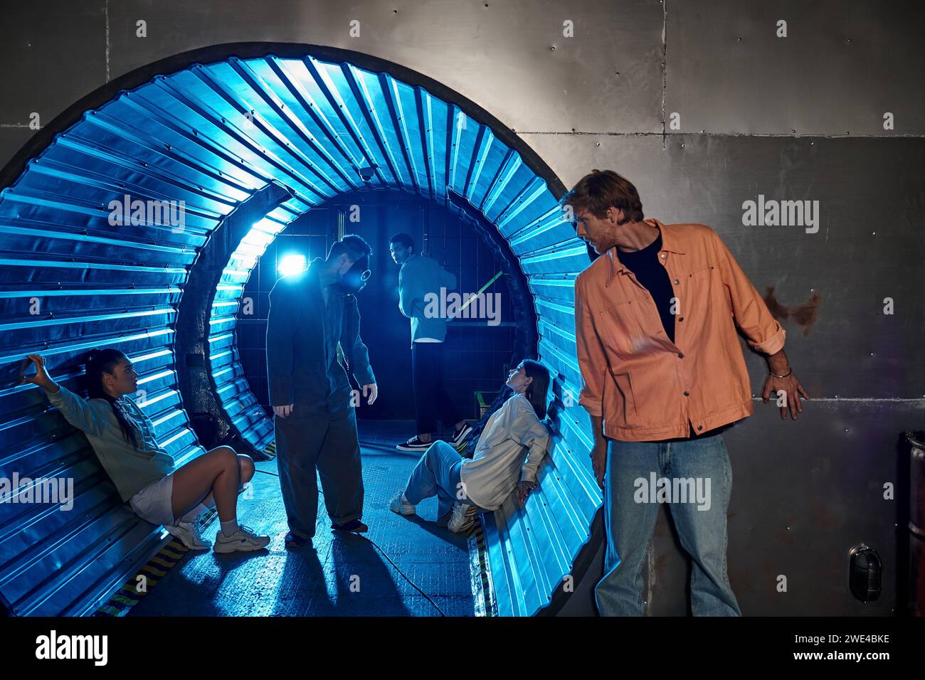 Interrassische Gruppe von Freunden, die an aufregenden Abenteuern im Quest Room teilnehmen, in einem Tunnel mit blauem Licht Stockfoto