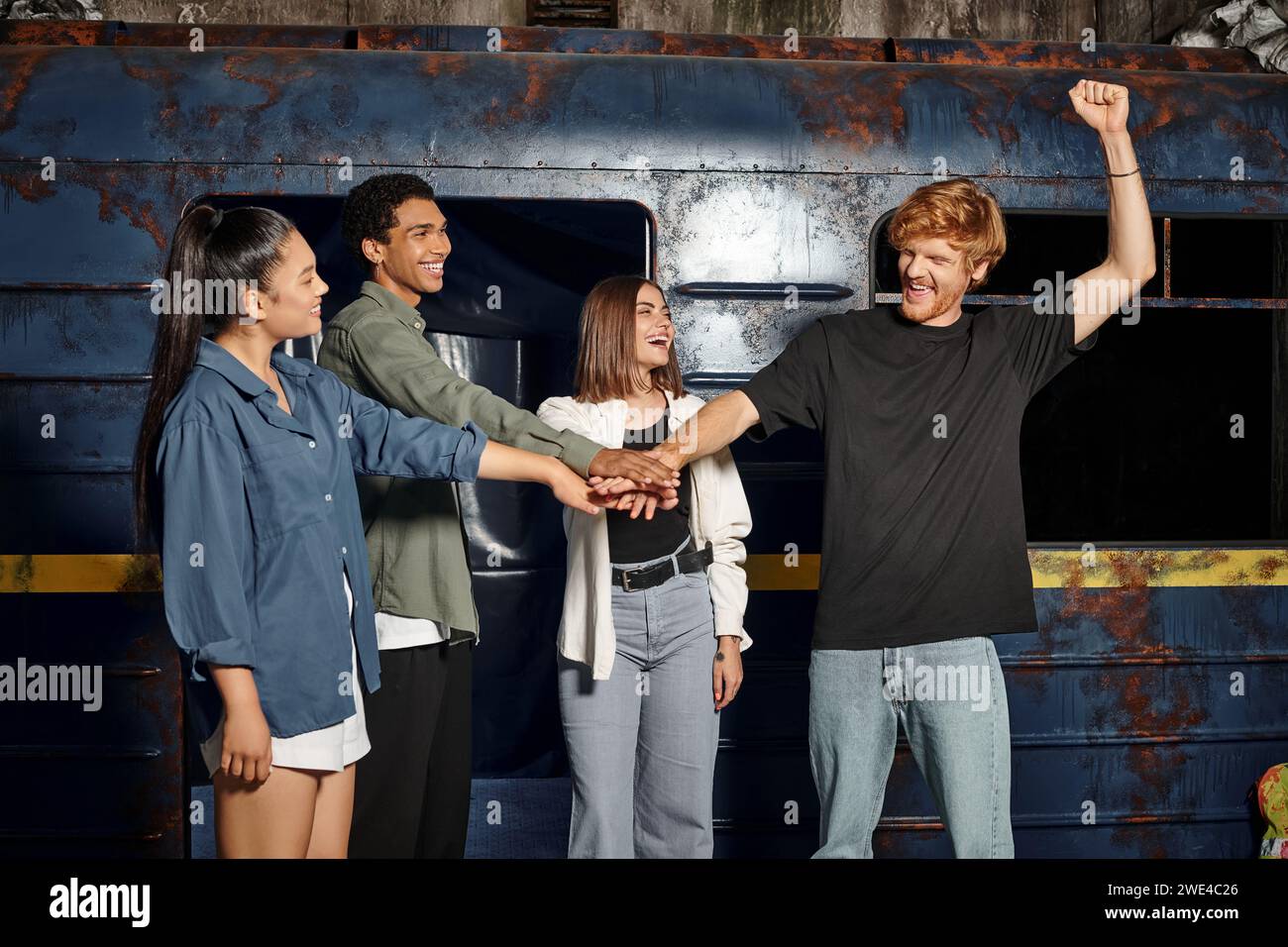 Aufregende junge multikulturelle Gruppe von Freunden, die Hände stapeln, während sie im städtischen Escape Room auf der Suche sind Stockfoto