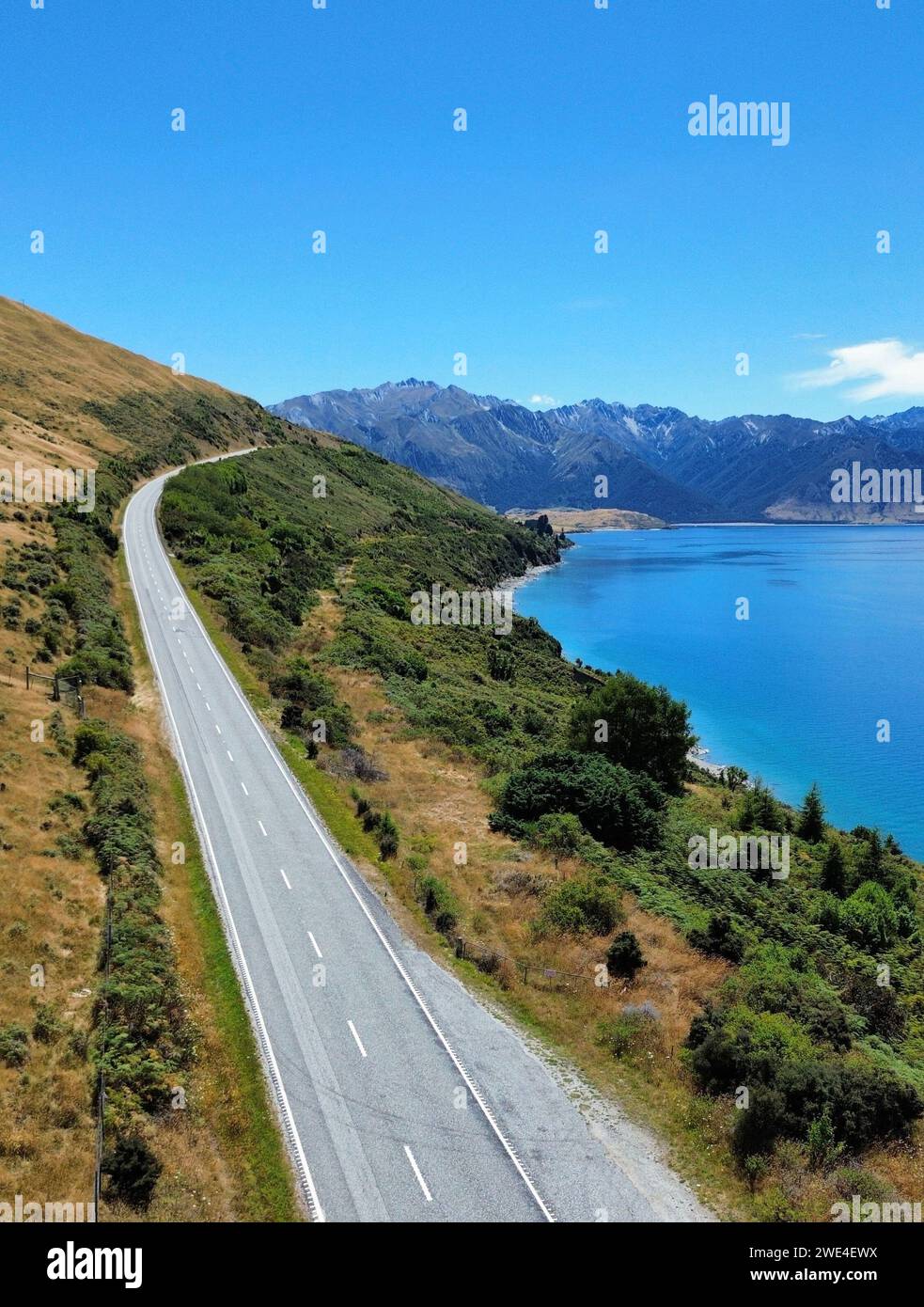 Ein Blick aus der Vogelperspektive auf eine Straße am Ufer des Lake Hawea, umgeben von üppigem Grün. Neuseeland Stockfoto