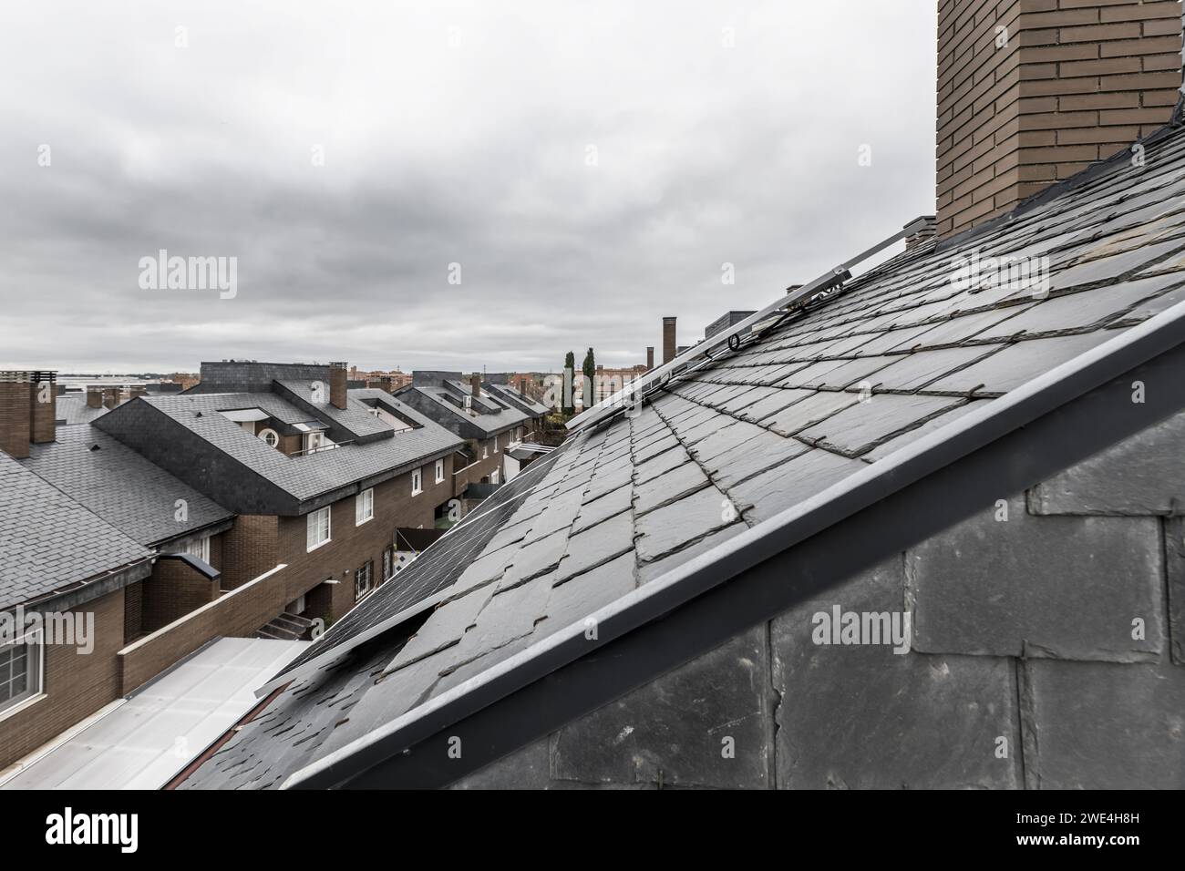 Dächer eines Wohnviertels mit schwarzen Schieferziegeln und Solarpaneelen auf den Dächern Stockfoto