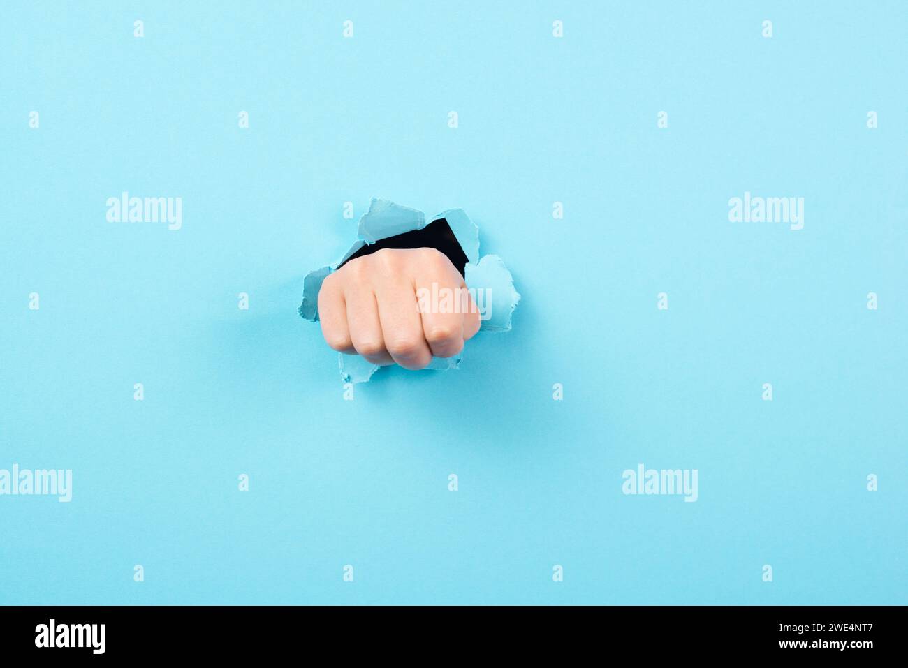 Die Faust bremst durch zerrissenes Papier, das Loch in den blauen Hintergrund locht, Konflikt-, Stress- und Kampfkonzept Stockfoto