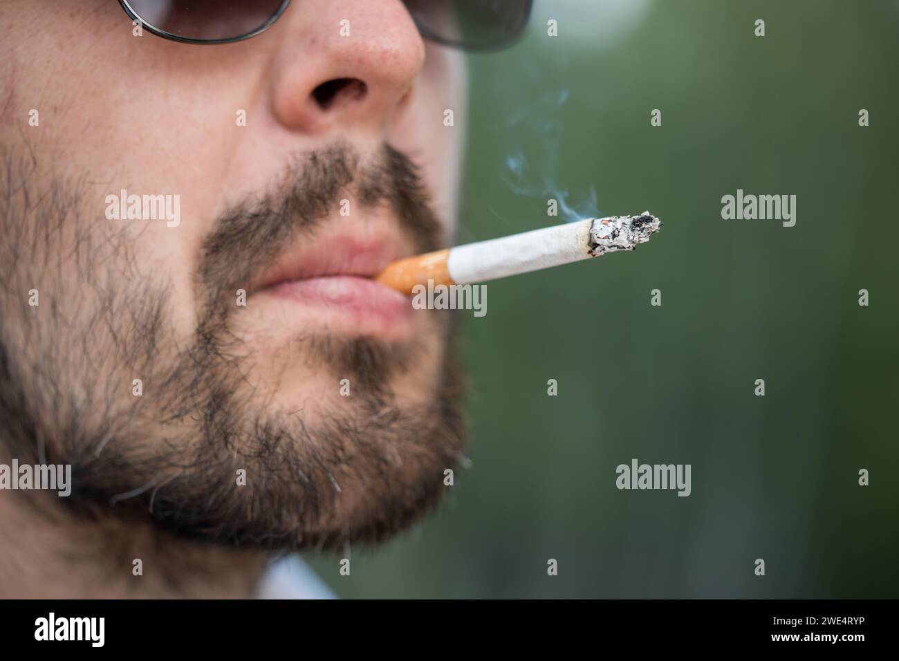 Nahaufnahme eines bärtigen Mannes in Sonnenbrille, der Zigarette raucht. Stockfoto