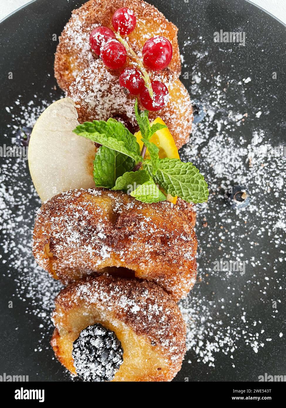 Apfelfritter auf dunklem Teller mit Zucker und Früchten. Stockfoto