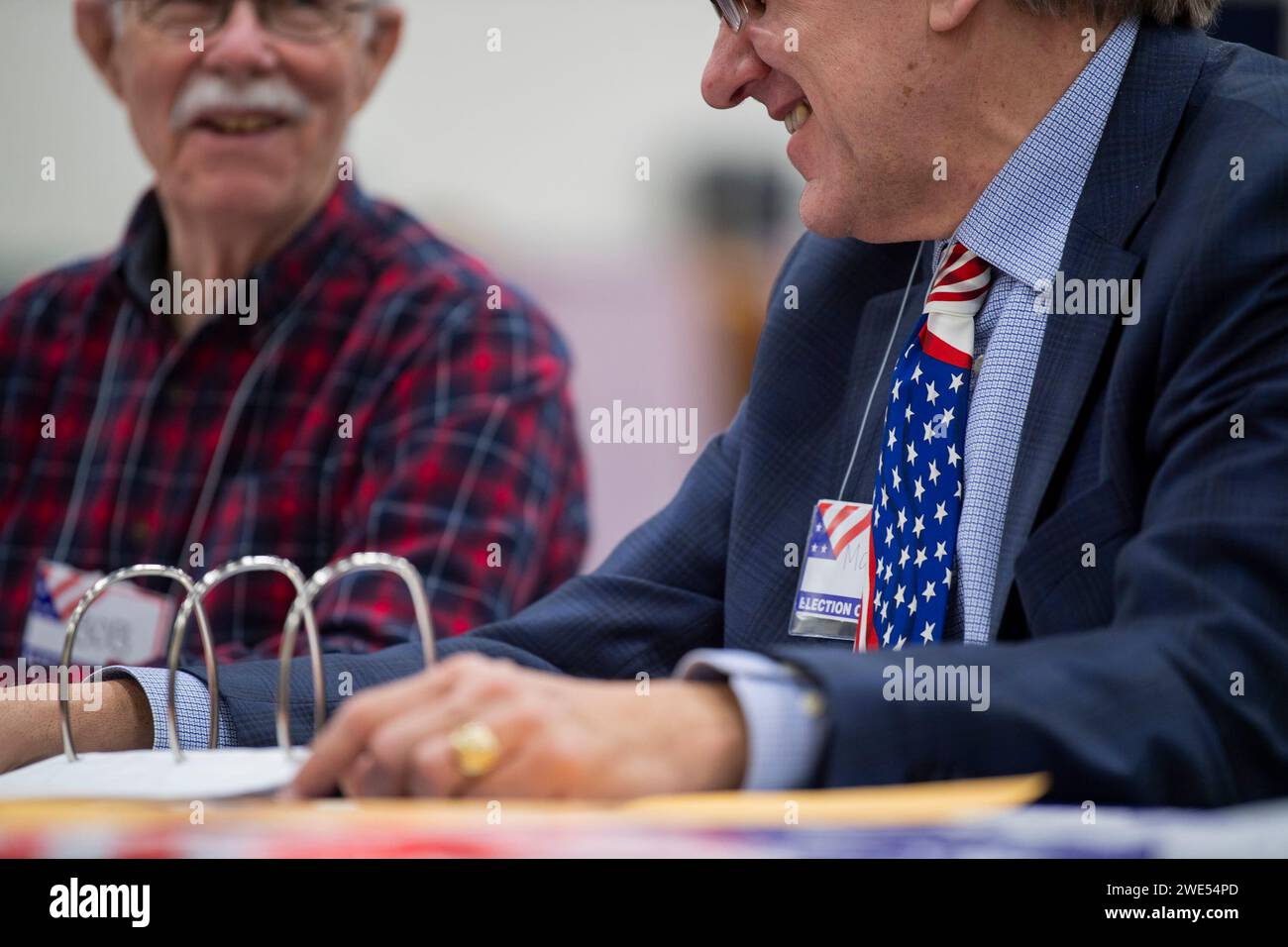 Windham, Usa. Januar 2024. Ein Wahlmitarbeiter, der eine amerikanische Flagge trägt, unterhält sich mit einem Kollegen, während die Leute am 23. Januar 2024 in der New Hampshire Primary an einer Wahlstelle an der Windham High School in Windham, New Hampshire, abstimmen. Der Republikaner Haley hofft, den ehemaligen US-Präsidenten Donald J. Trump bei den Umfragen in New Hampshire zu besiegen, während der Demokrat Dean Phillips hofft, an Dynamik gegen Präsident Joe Biden gewinnen zu können . Foto: Amanda Sabga/UPI Credit: UPI/Alamy Live News Stockfoto