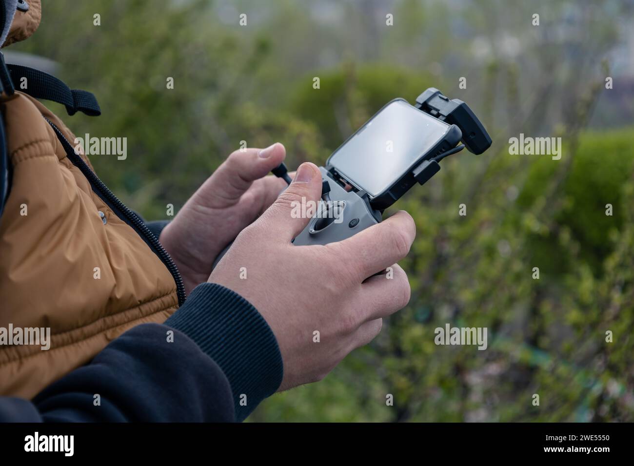 Männliche Hände halten ein Drohnenbedienfeld mit angeschlossenem Telefon, Nahaufnahme. Management durch Quadcopterflug und Videotaping von oben. Frühling im Freien. Stockfoto