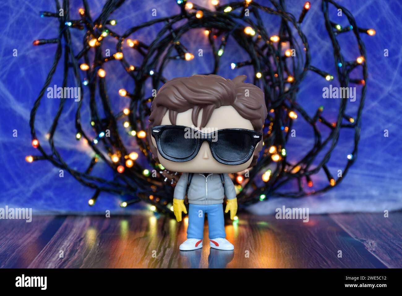 Funko Pop Actionfigur von Steve mit Sonnenbrille aus der beliebten Netflix TV-Serie Stranger Things. Blauer nebeliger Hintergrund, bunte Lichter, gespendet. Stockfoto