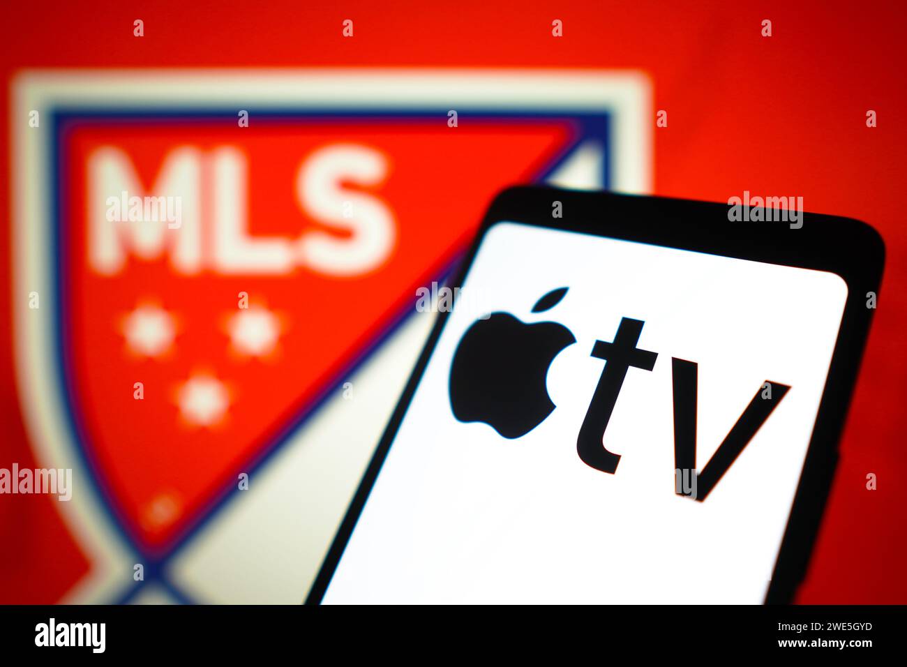 In dieser Fotoabbildung wird das Apple TV-Logo auf einem Smartphone-Bildschirm und das Major League Soccer (MLS)-Logo im Hintergrund angezeigt. Stockfoto