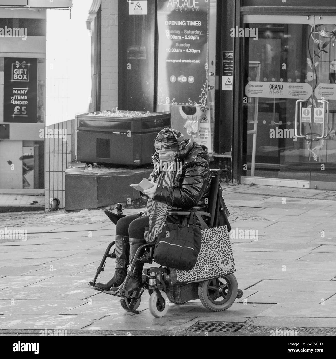 17.01.2024 Wigan, Greater Manchester, Großbritannien. Frau mit Gesichtsmaske und Kopftuch auf einem Rollstuhl Stockfoto