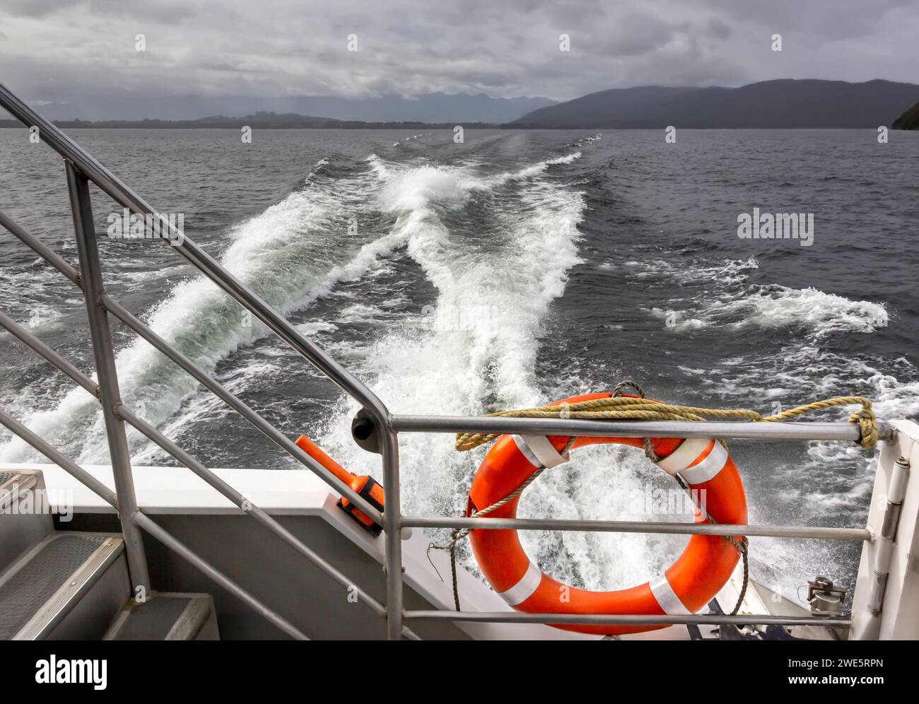 Ein Notfall-orangener Rettungsboje-Ring und die fließende Dynamik eines Aufwachs hinter einer Passagierfähre des Katamarans über den Manapouri-See in Neuseeland. Stockfoto