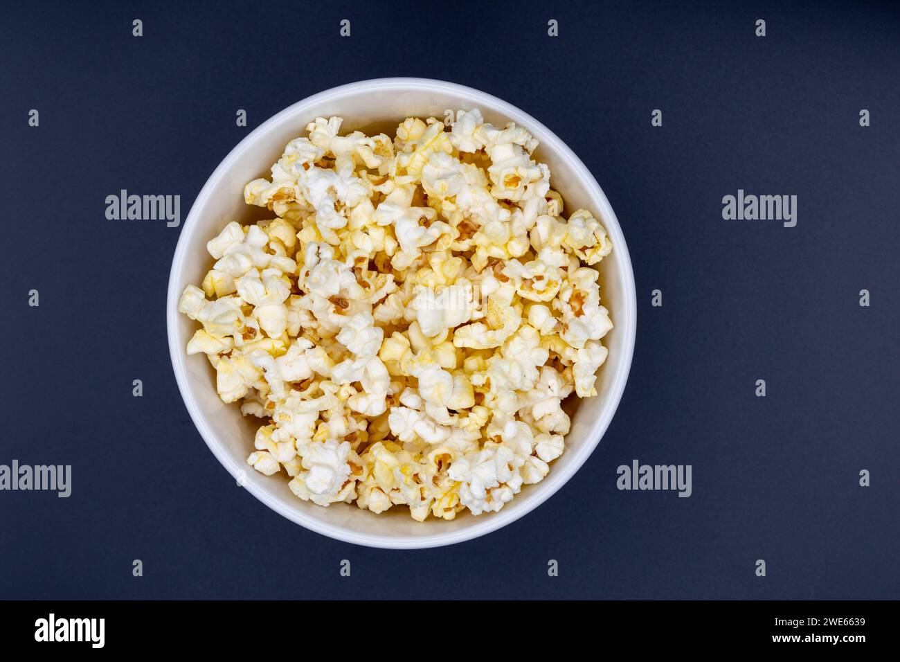 Weiße Schüssel mit Mikrowellen-Popcorn vor schwarzem Hintergrund Stockfoto