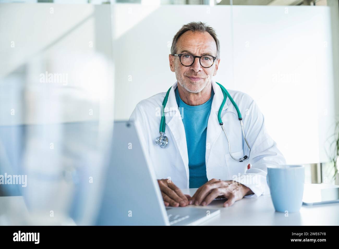 Lächelnder Seniorarzt sitzt am Schreibtisch Stockfoto