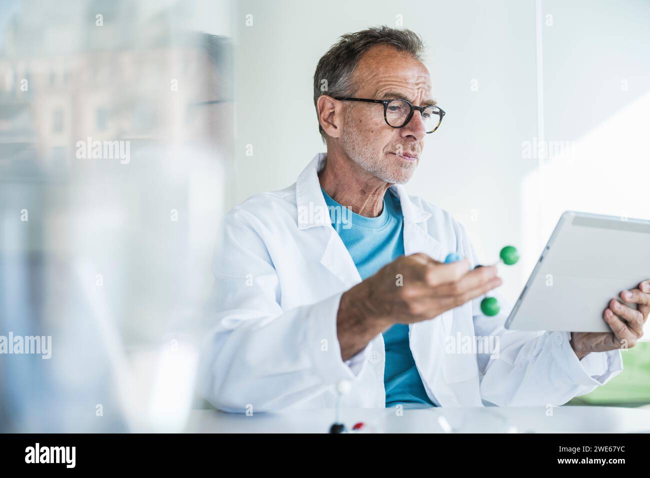 Mann im Labormantel mit Molekularstruktur und Tablet-PC am Schreibtisch Stockfoto
