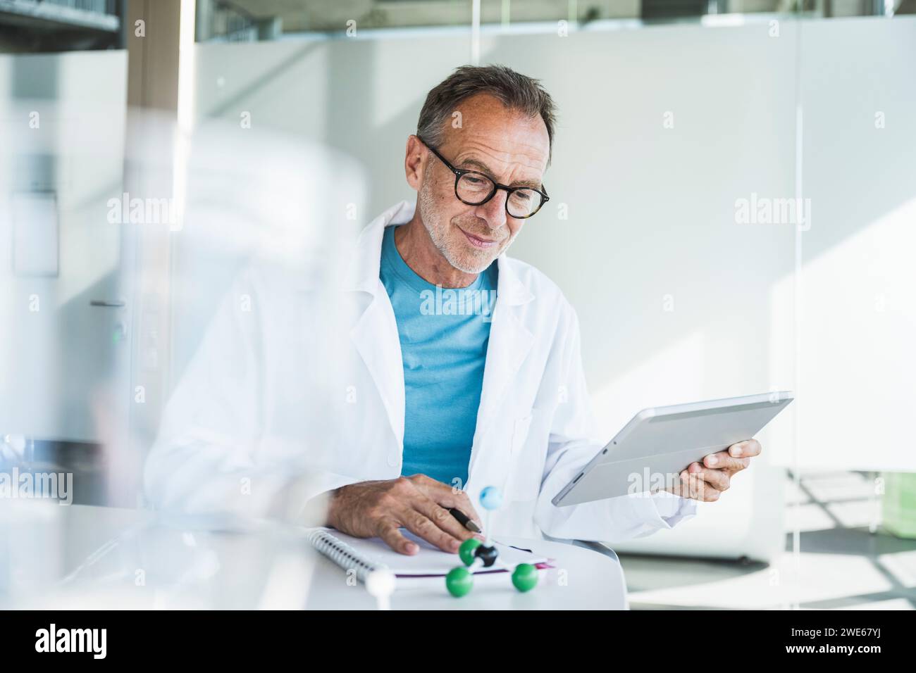 Lächelnder Seniorarzt mit Tablet-PC und Notizblock am Schreibtisch Stockfoto