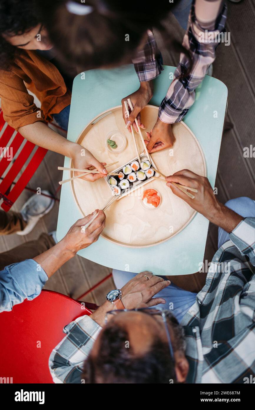 Hände von multikulturellen Freunden, die Sushi mit Essstäbchen essen Stockfoto