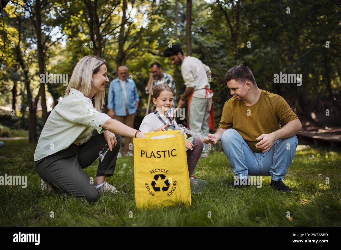 Sozial inkludierende Gruppe von Freiwilligen, die Kunststoffabfälle in Recyclingbeutel legen Stockfoto