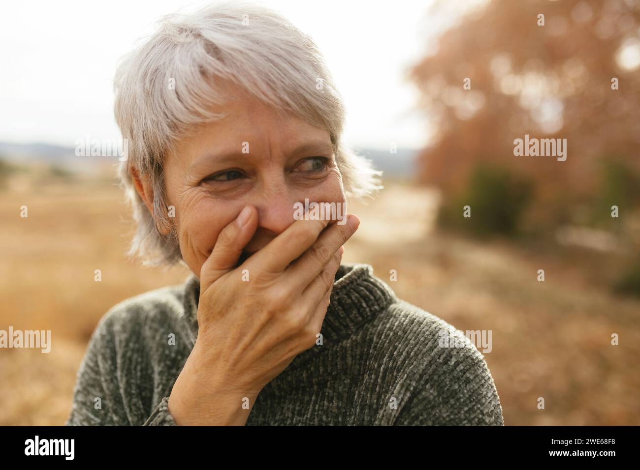 Glückliche Frau mit grauen Haaren, die den Mund bedeckt und lacht Stockfoto