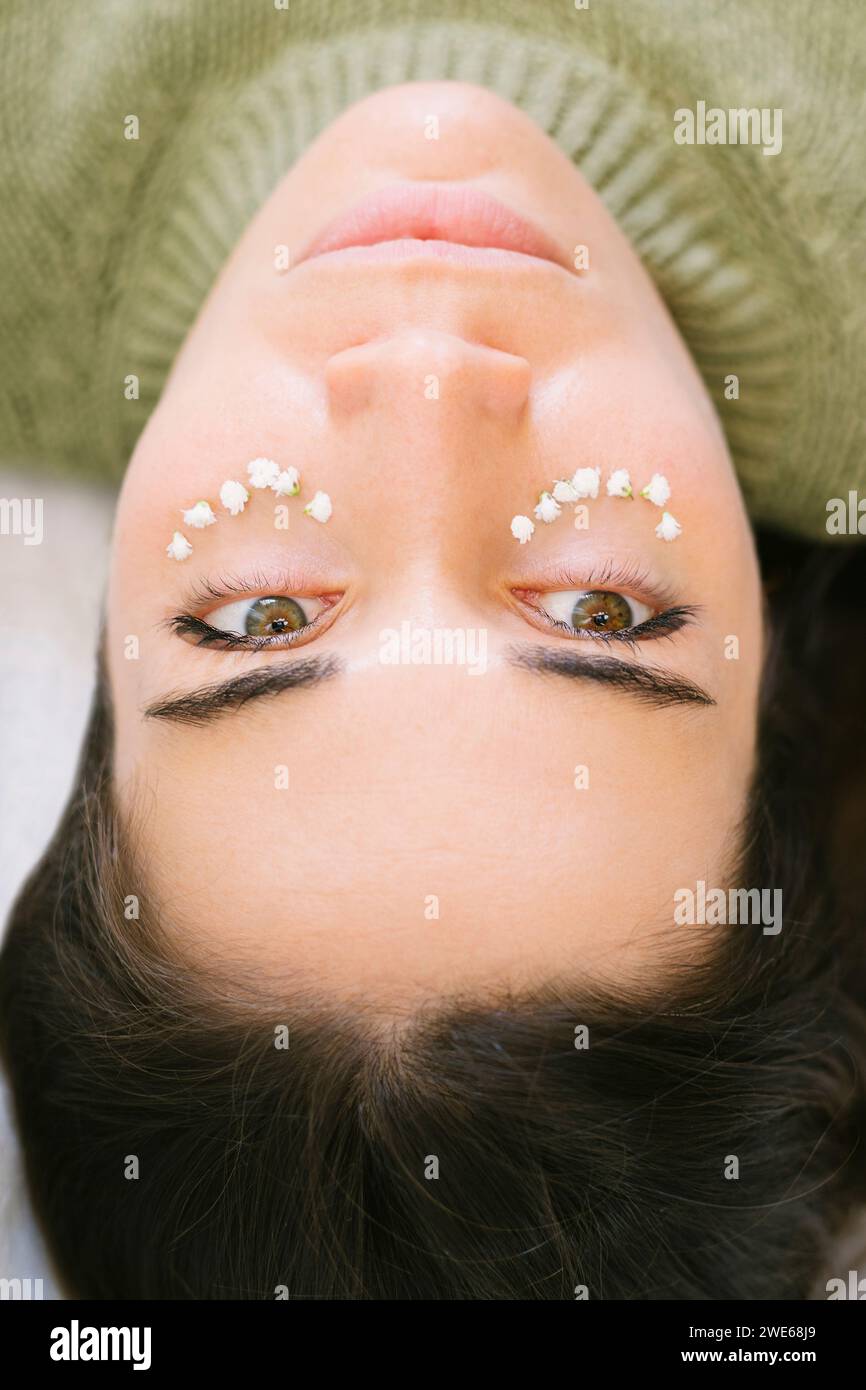 Schöne Frau, die mit Blumen unter den Augen liegt Stockfoto