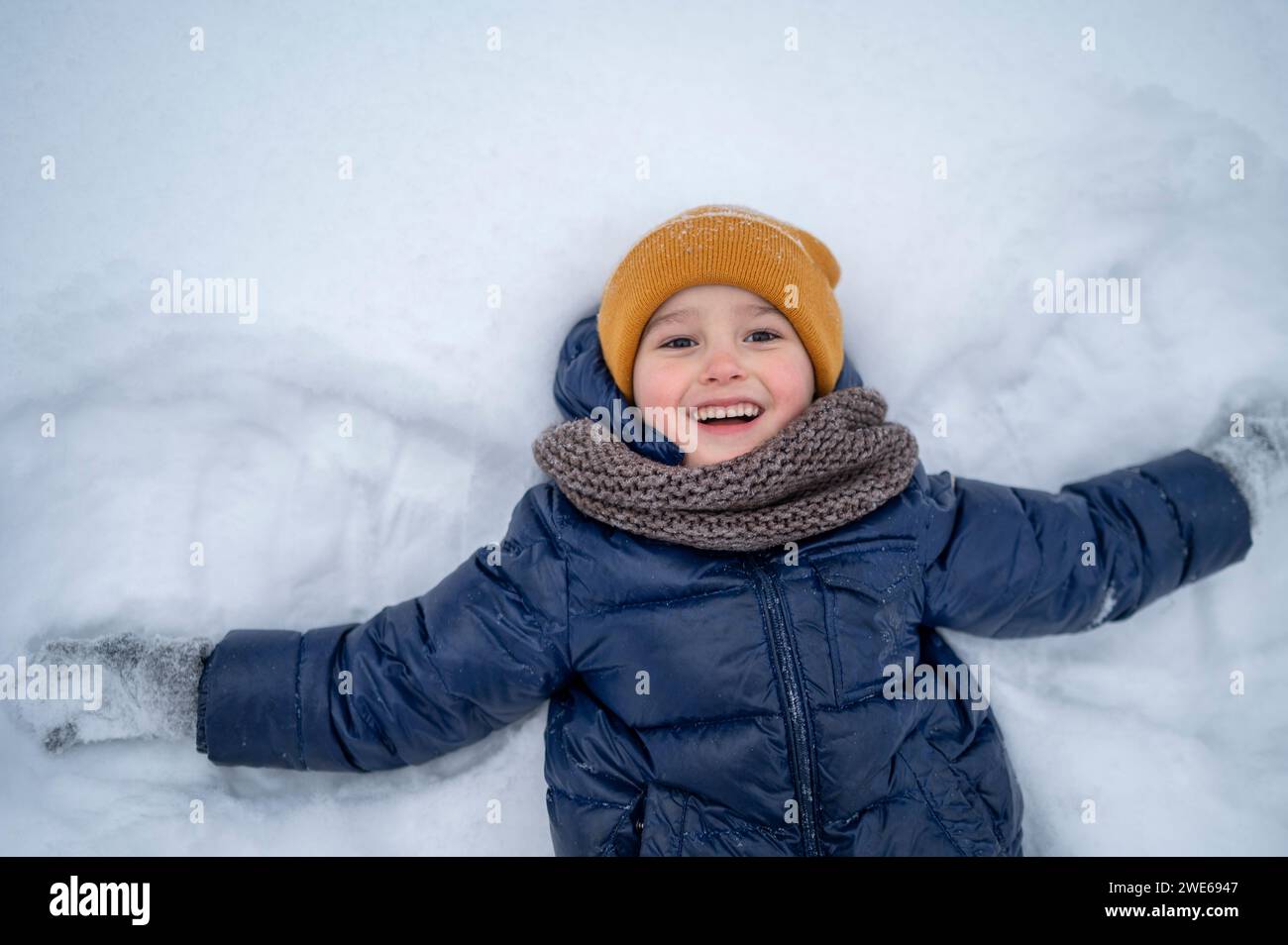 Lächelnder Junge, der im Winter im Schnee liegt Stockfoto