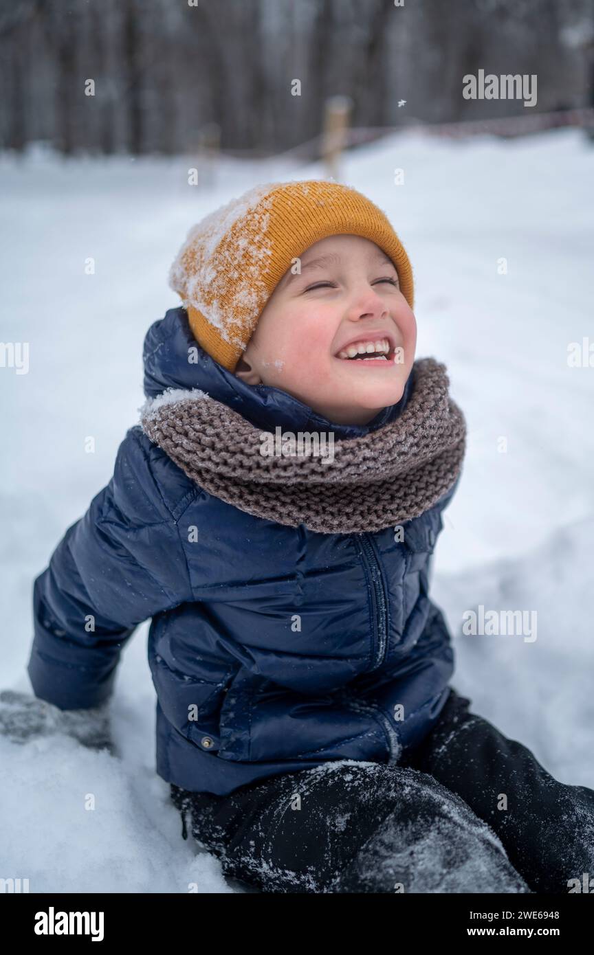 Junge sitzt im Schnee und lacht im Winterpark Stockfoto