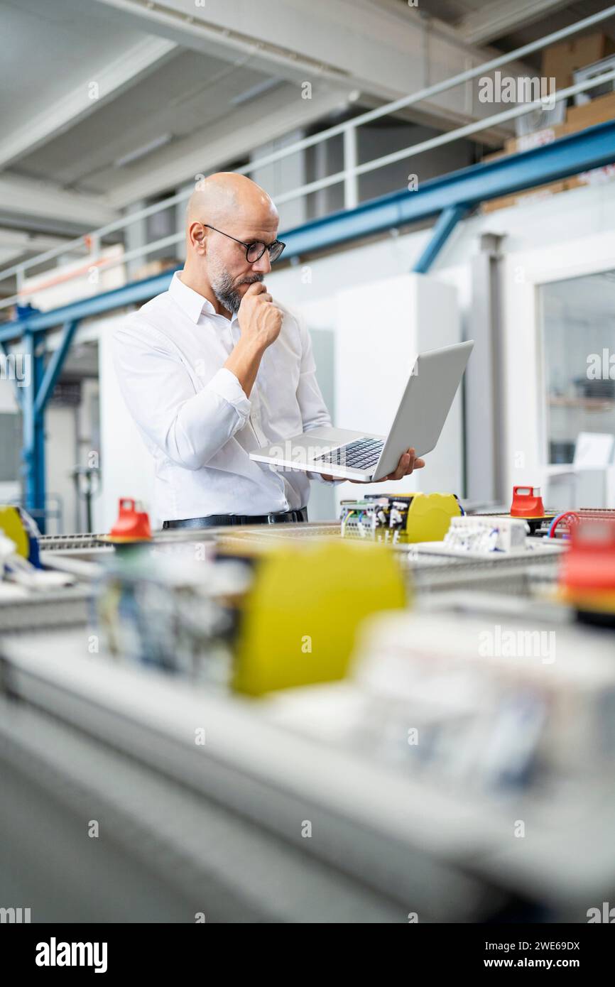 Geschäftsmann plant und benutzt Laptop in der Nähe von Maschinen in der Fabrik Stockfoto