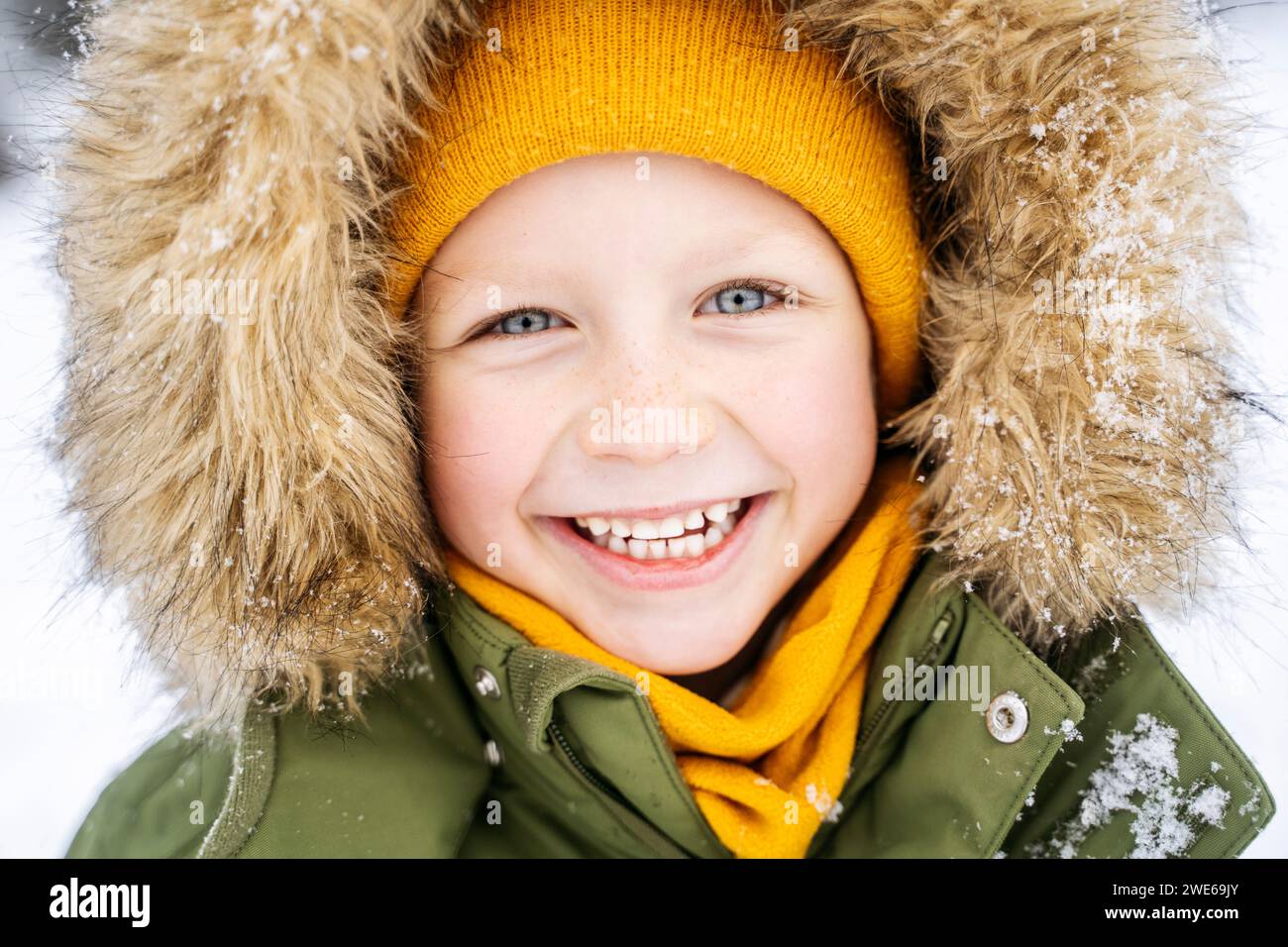 Glücklicher Junge, der im Schnee einen Mantel trägt Stockfoto