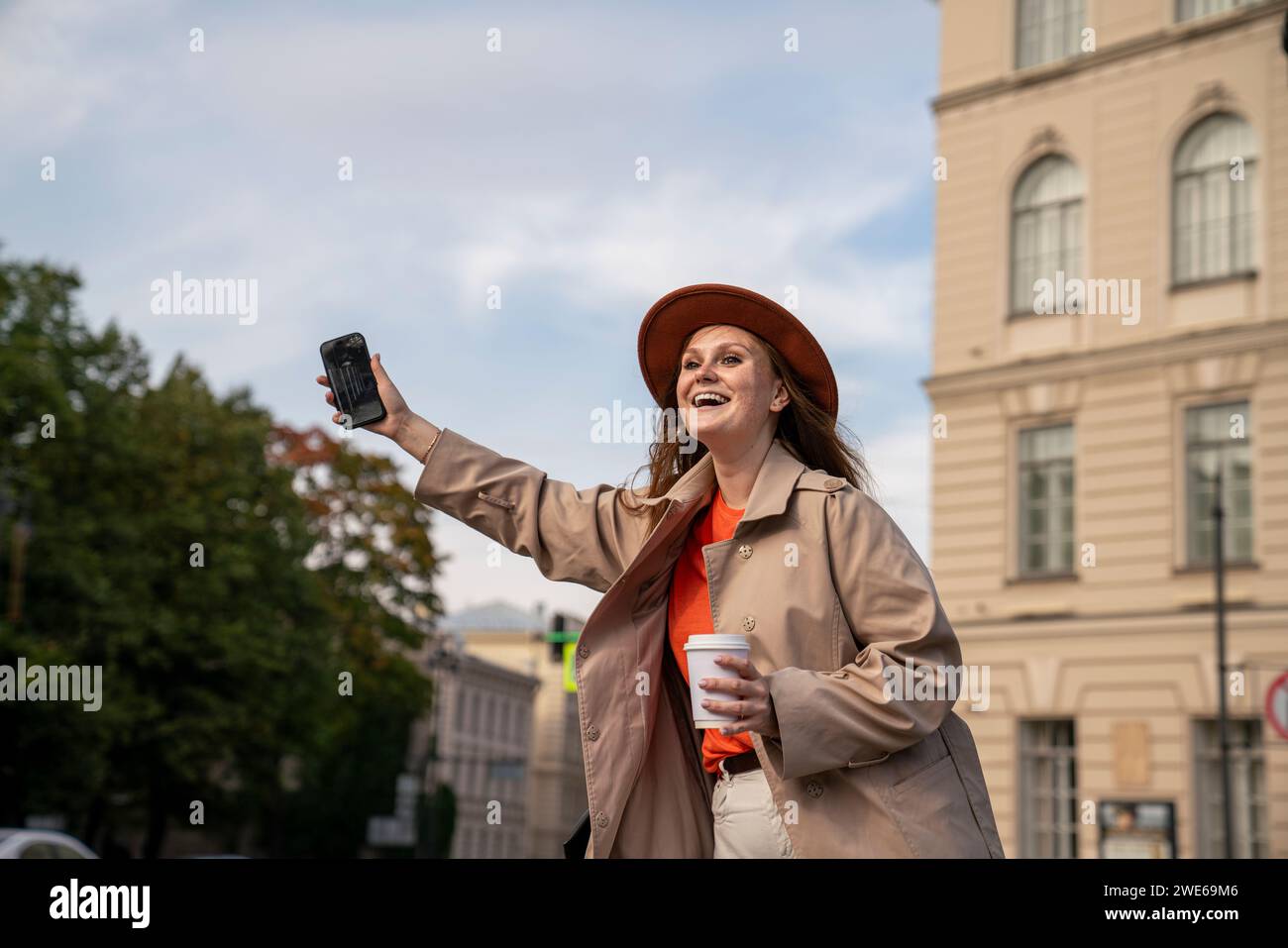 Glückliche Frau, die ihr Smartphone hält und in der Nähe des Gebäudes fährt Stockfoto