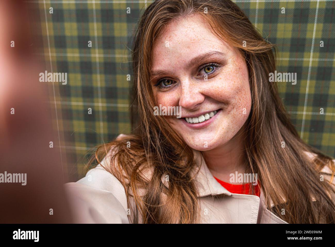 Lächelnde Frau macht Selfie vor einer karierten Musterwand Stockfoto