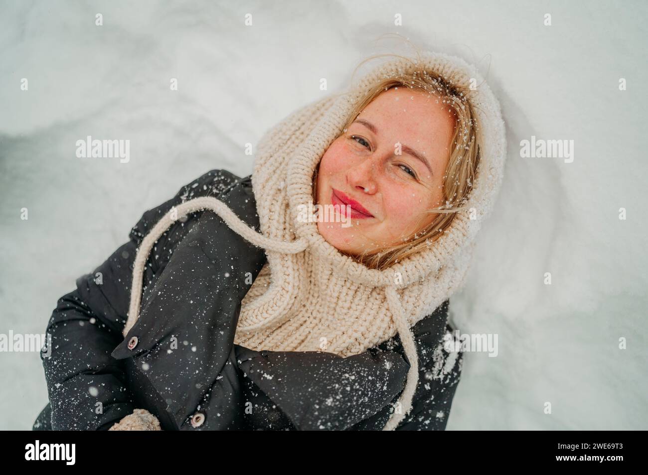 Glückliche junge Frau, die auf Schnee liegt Stockfoto