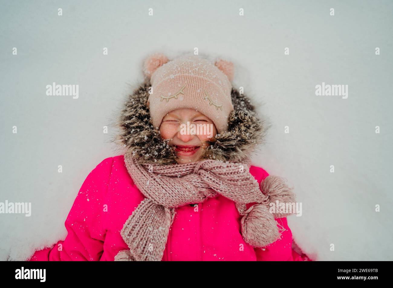 Lächelndes Mädchen, das im Winter auf Schnee liegt Stockfoto