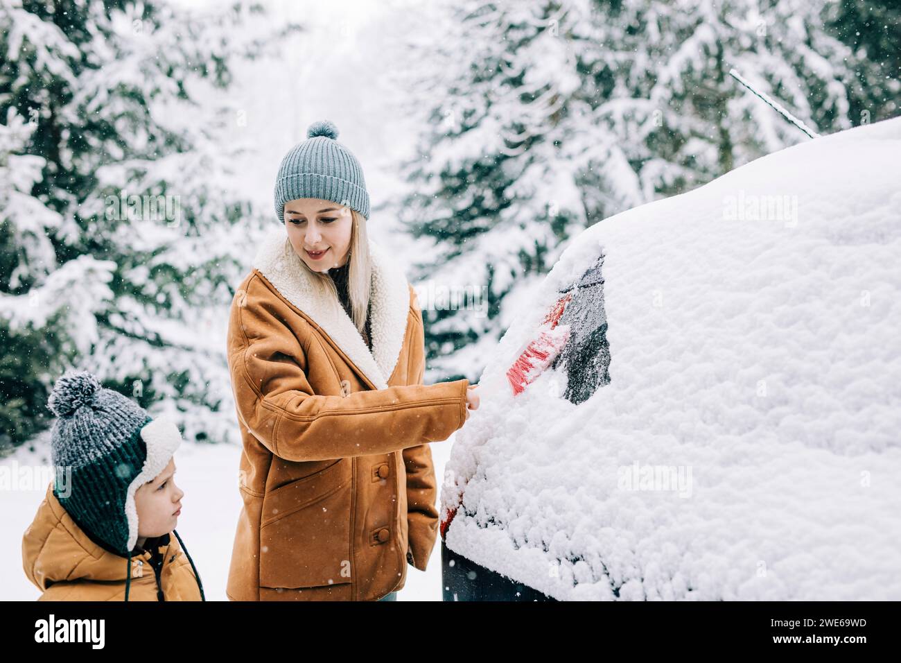 Frau räumt mit einem Besen Schnee aus einem Auto 4543490 Stock