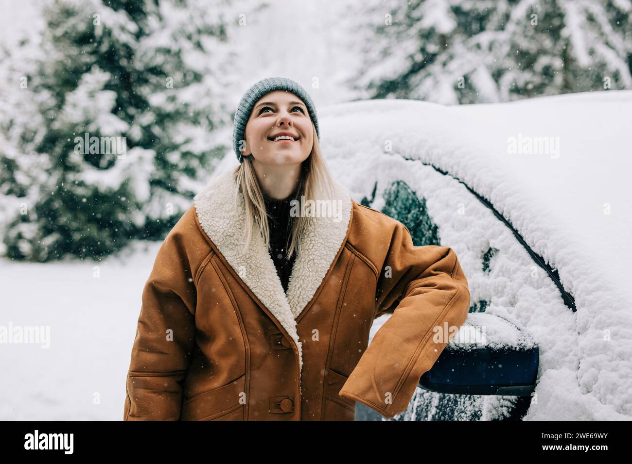 Frau im Wintermantel und lehnt sich im Schnee auf das Auto Stockfoto