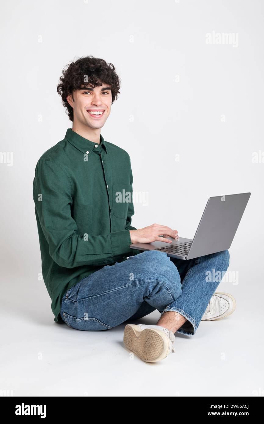 Lächelnder Mann, der mit Laptop vor weißem Hintergrund sitzt Stockfoto