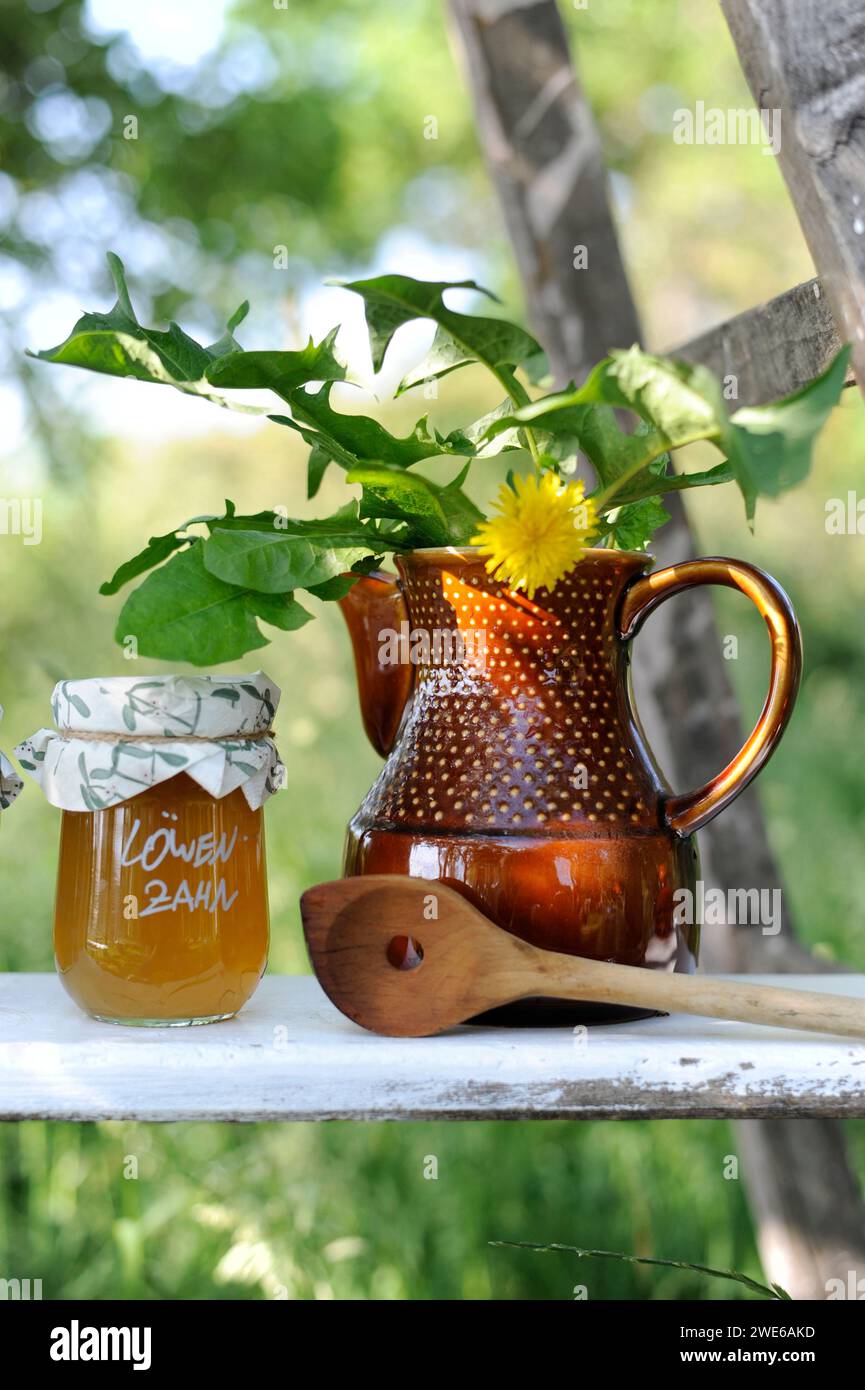 Ein Glas Marmelade, eine Holzkelle und ein Löwenzahn in einem Keramikkrug Stockfoto
