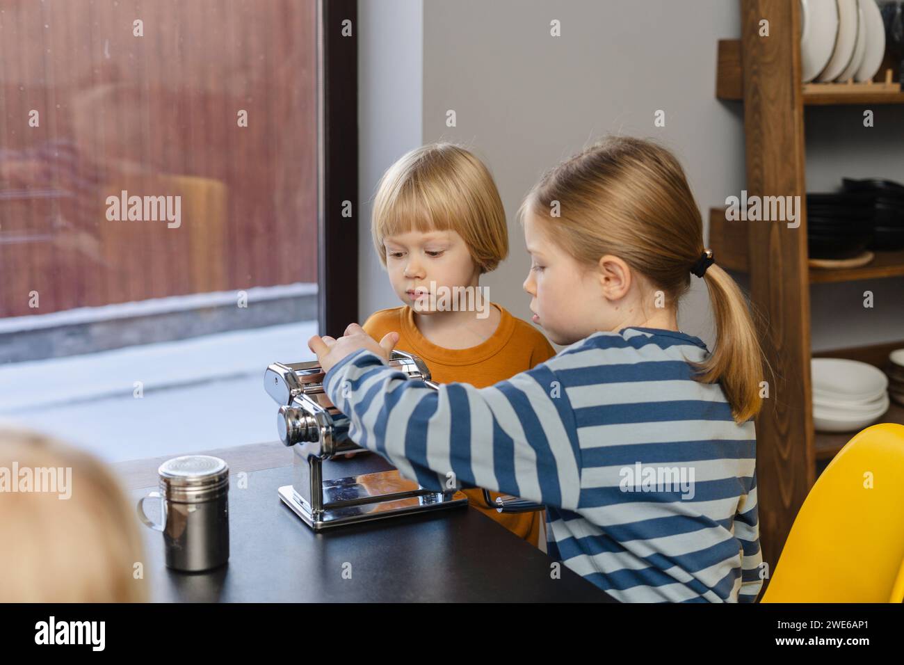 Mädchen und Junge sitzen mit Nudelmacher am Esstisch Stockfoto