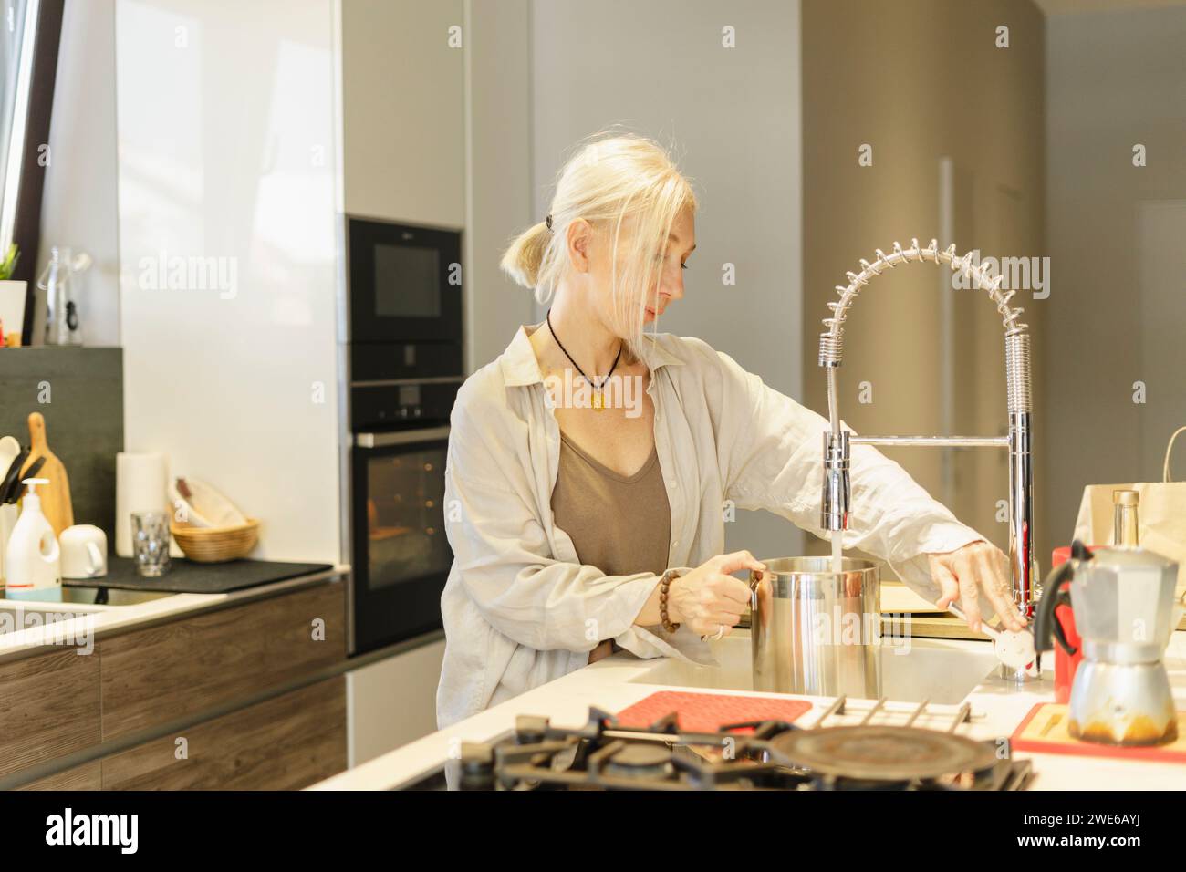 Reife Frau füllt Stahlkrug mit Wasser in der Küche zu Hause Stockfoto
