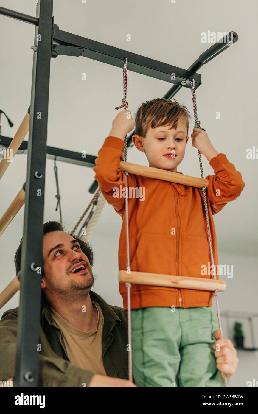 Der lächelnde Vater bringt dem Sohn bei, zu Hause auf eine Seilleiter zu klettern Stockfoto