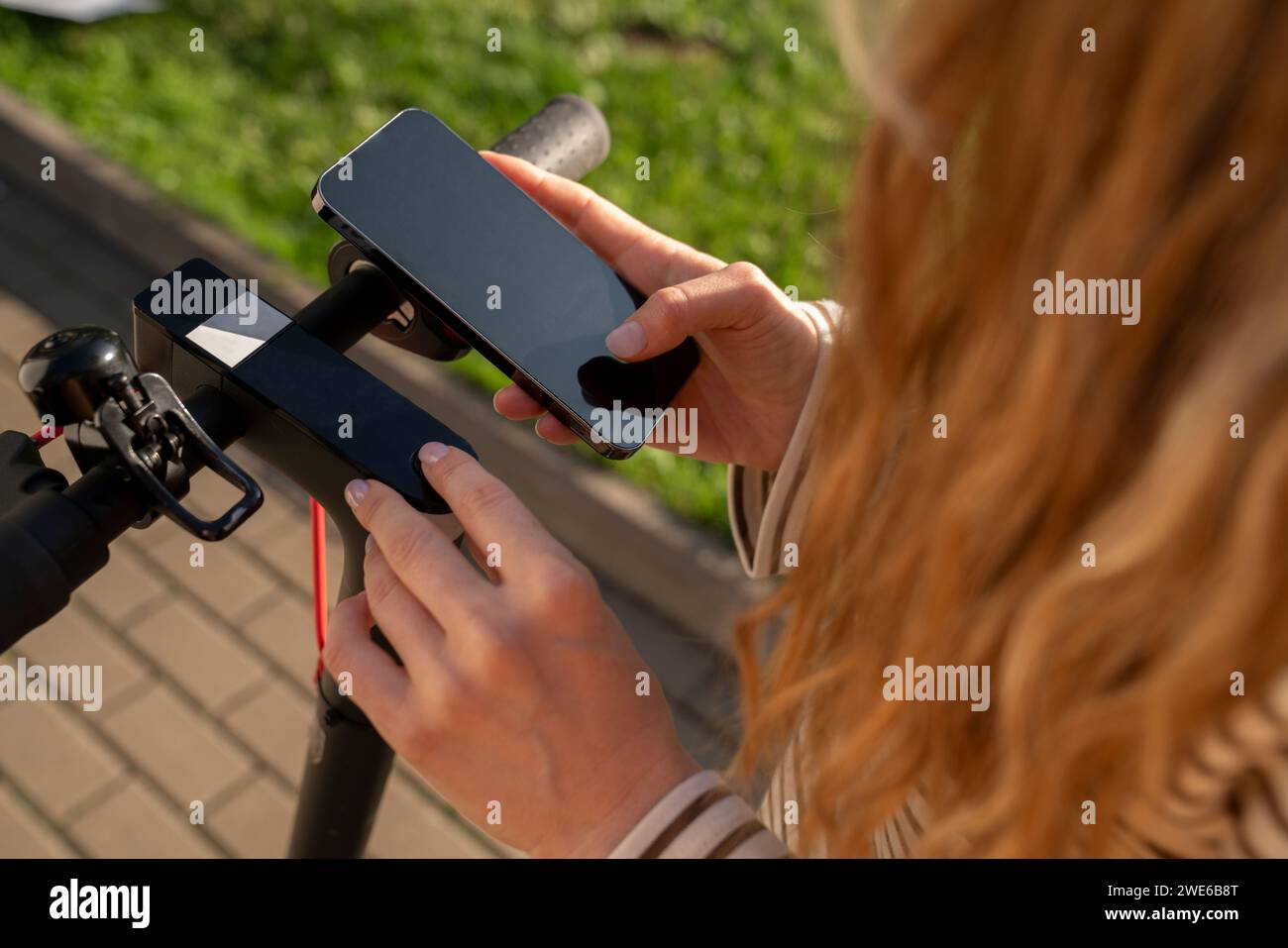 Frau scannt mit Handy über elektrischen Roller Stockfoto