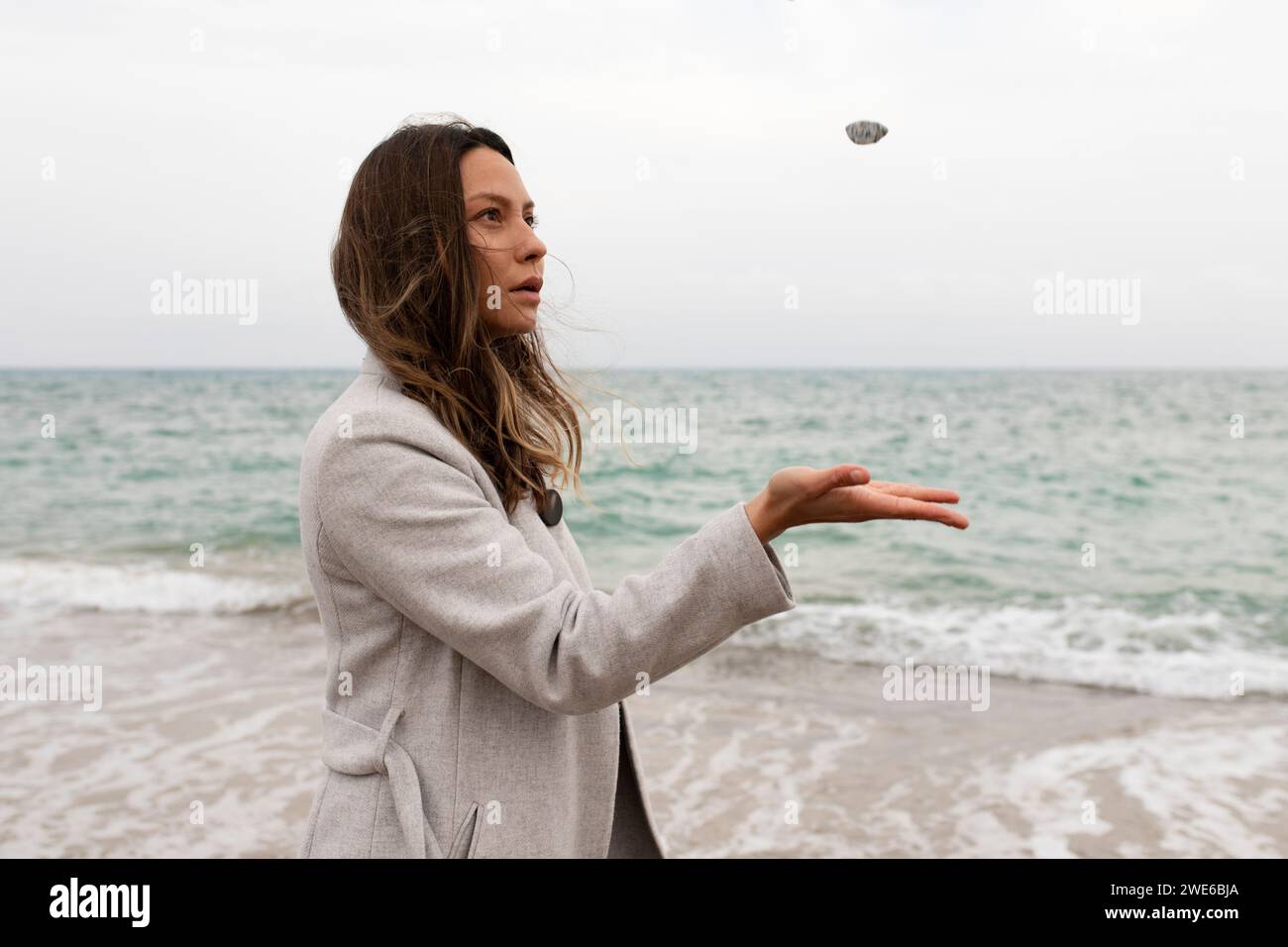 Frau, die Kieselstein in der Nähe des Meeres am Strand fängt Stockfoto
