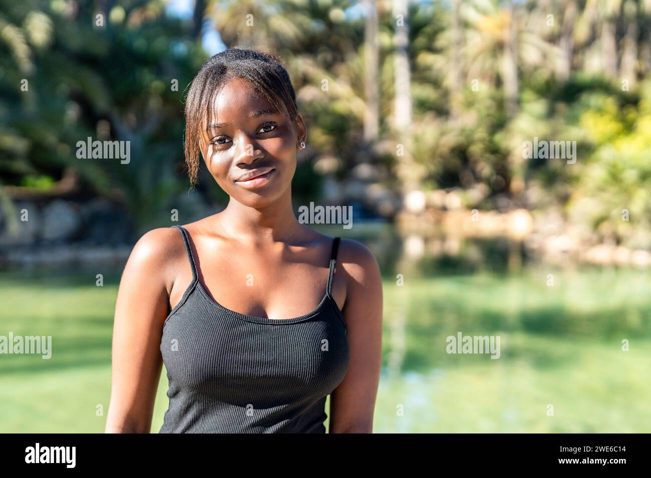 Lächelnde Frau mit schwarzem Tanktop im Park an sonnigem Tag Stockfoto