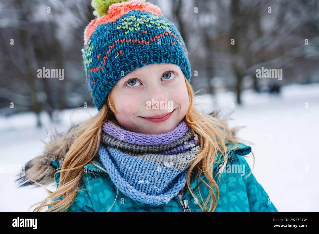 Lächelndes blondes Mädchen mit Schal und Strickmütze im Winter Stockfoto