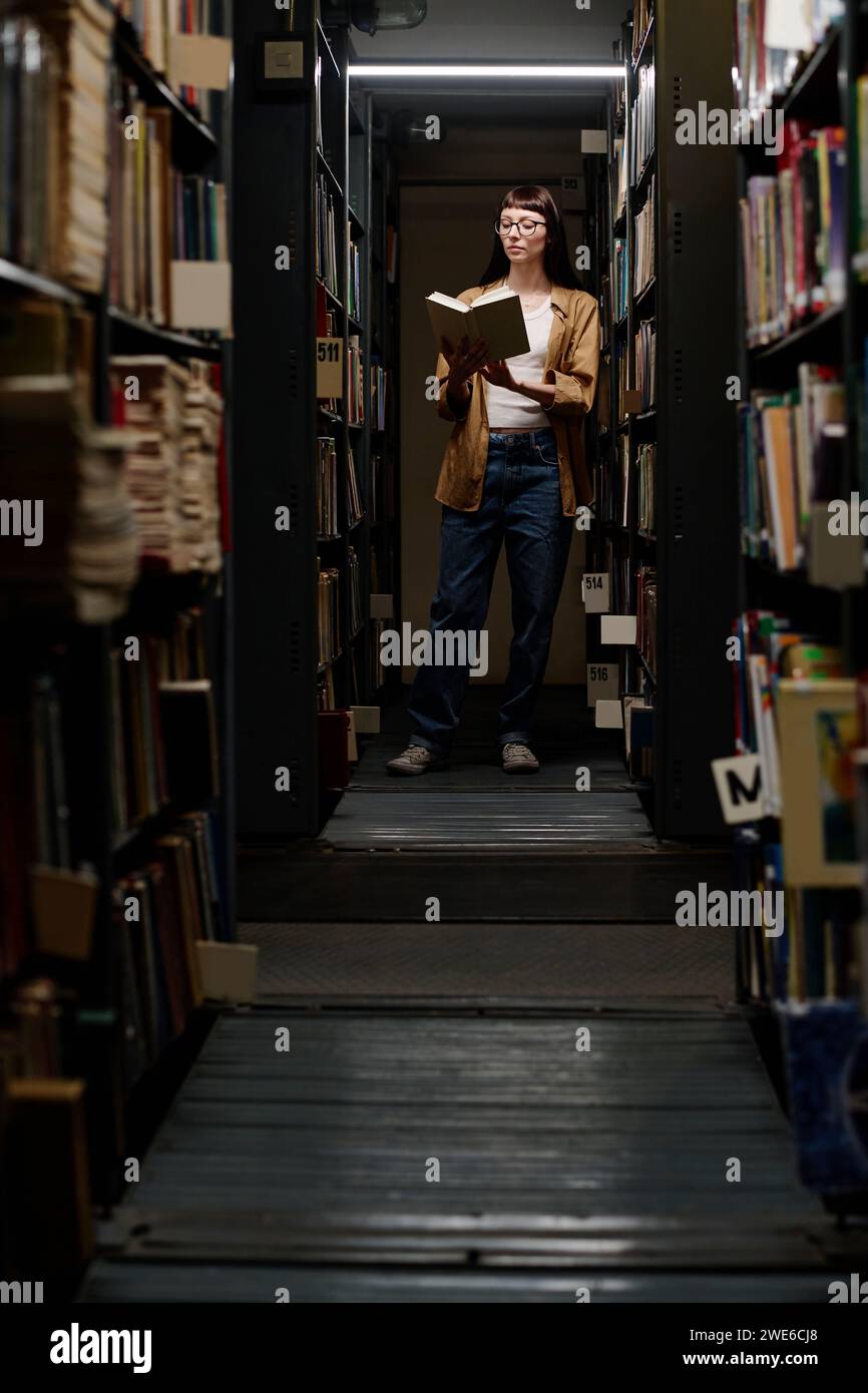 Junge Studentin, die Bücher in Bücherregalen liest Stockfoto