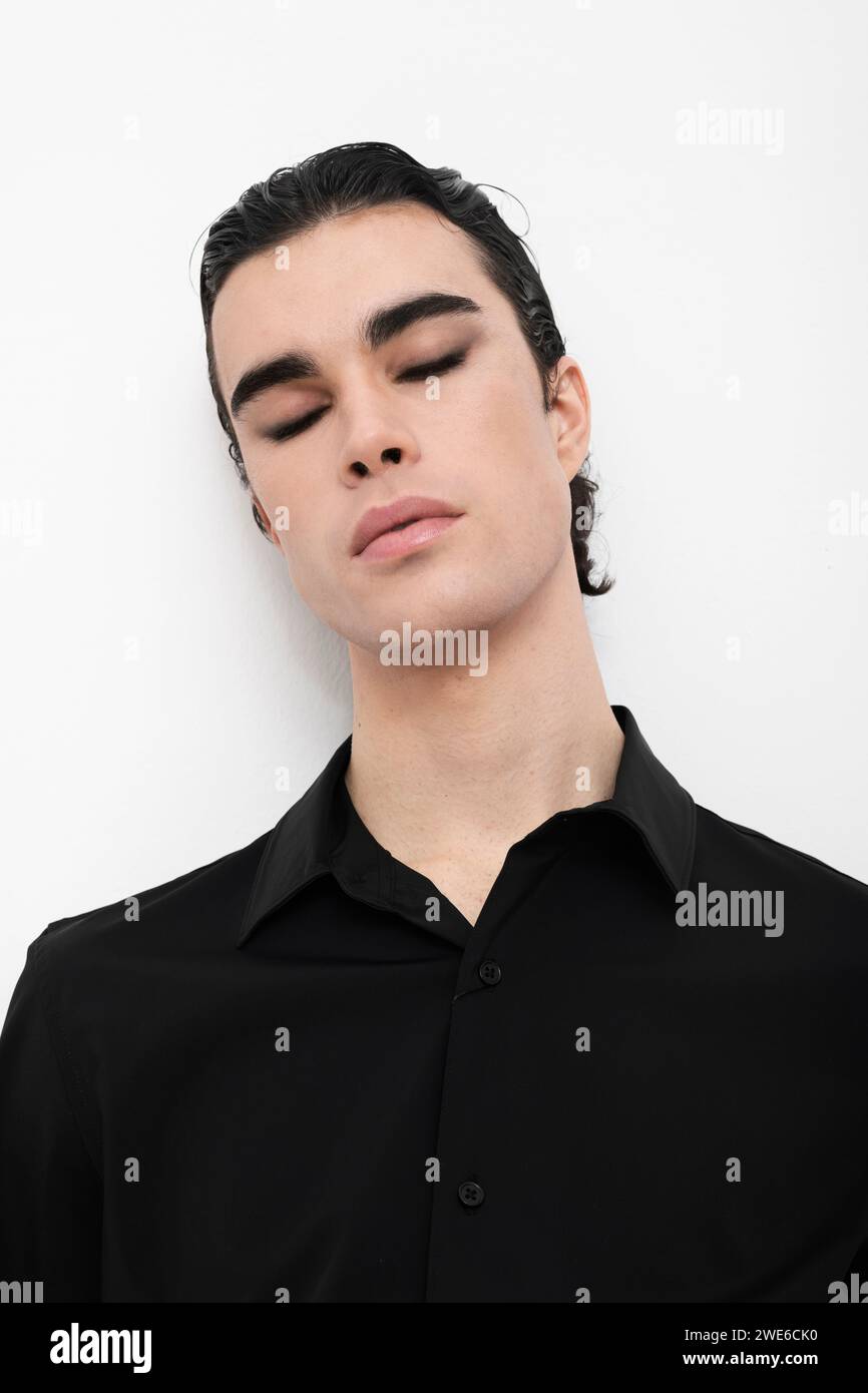 Junger Mann mit geschlossenen Augen, der ein schwarzes Hemd auf weißem Hintergrund trägt Stockfoto