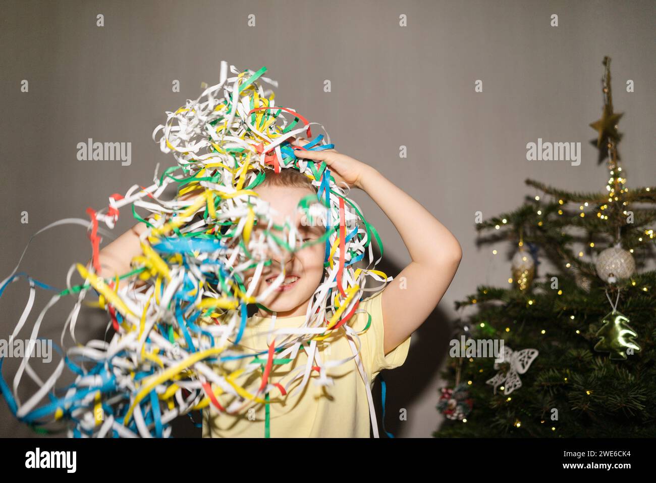 Fröhlicher Junge, der mit Partypoppern in der Nähe des Weihnachtsbaums zu Hause spielt Stockfoto