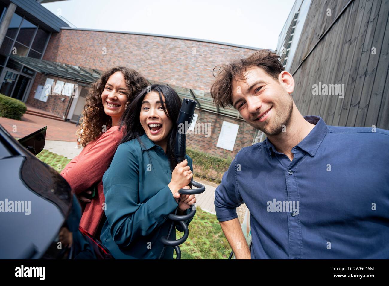 Glückliche multirassische Freunde stehen am Elektroauto Stockfoto