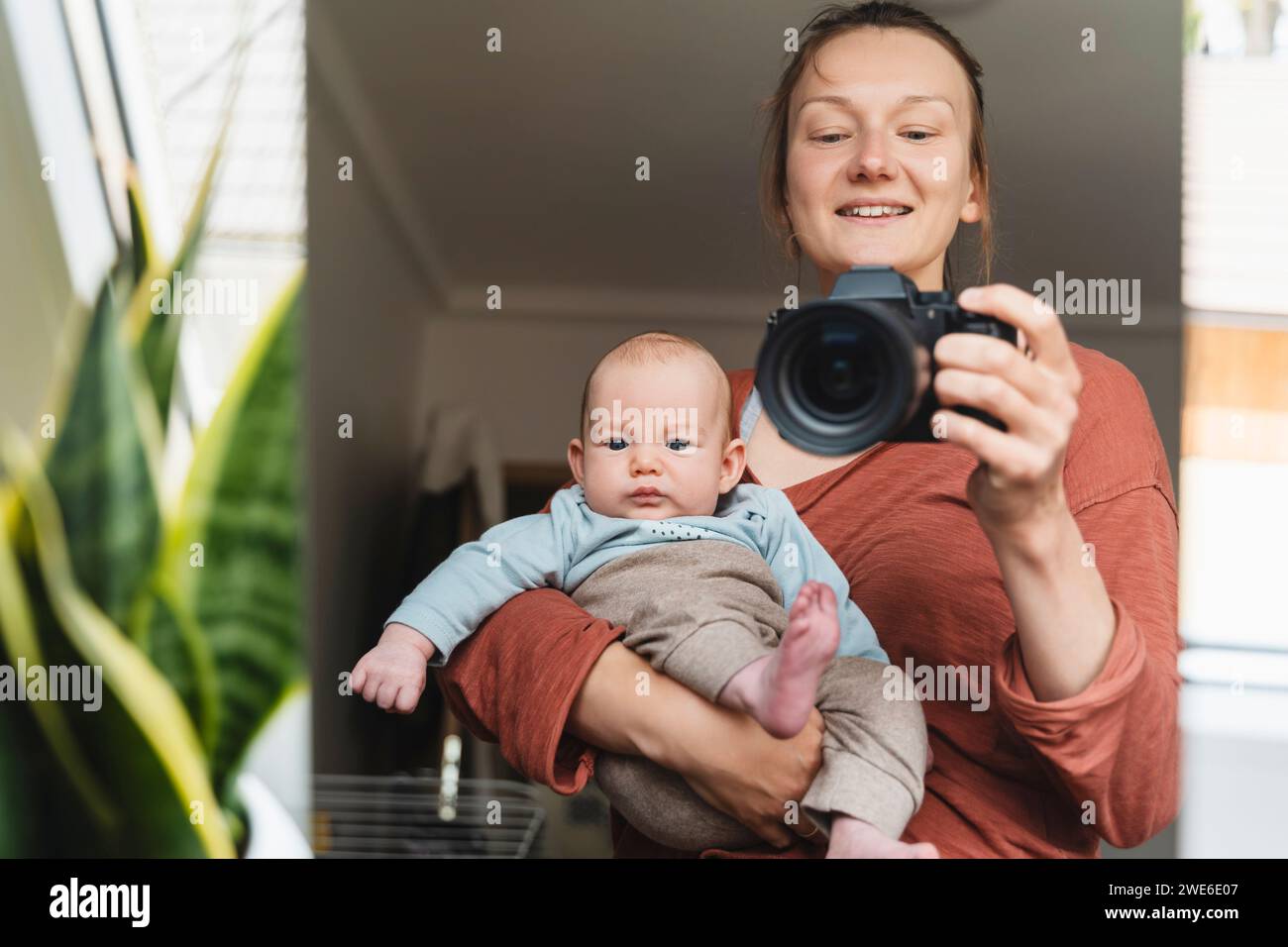 Reflexion einer lächelnden Mutter, die den Sohn trägt und durch die Kamera fotografiert Stockfoto