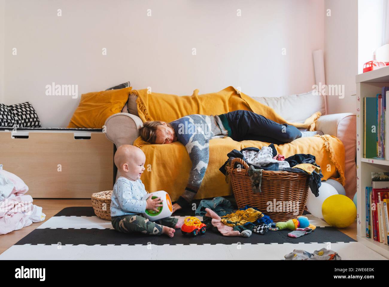 Erschöpfte Mutter, die auf dem Sofa schläft, während der Junge zu Hause spielt Stockfoto