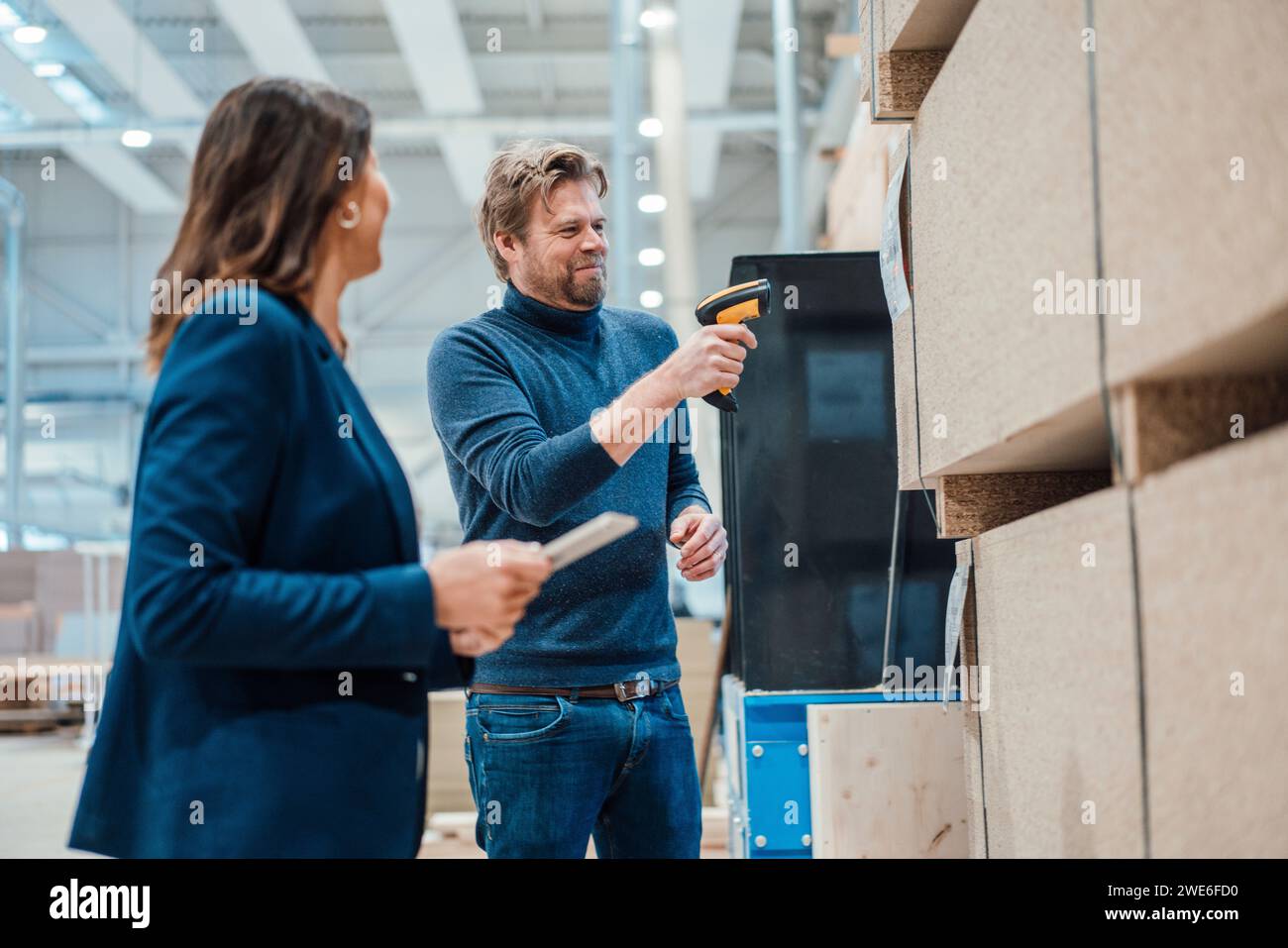 Lächelnder Geschäftsmann, der Barcode auf Holzdielen scannt, von einem Kollegen aus der Industrie Stockfoto