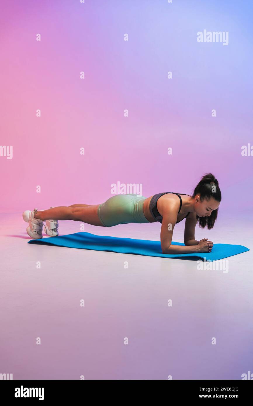 Junge Frau, die Plank-Position auf Yogamatte vor farbigem Hintergrund ausübt Stockfoto