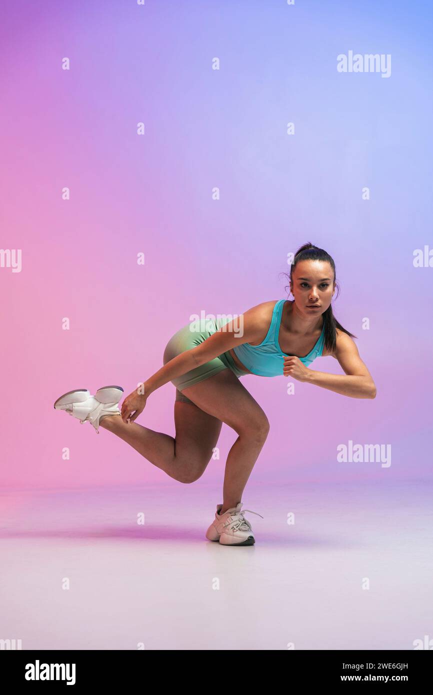 Selbstbewusste junge Frau, die auf einem Bein vor farbigem Hintergrund trainiert Stockfoto
